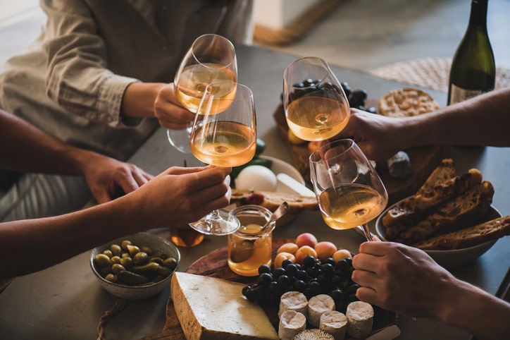 Couple of friends sitting around a dinner table having a toast with wine glasses.