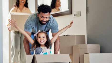 A father pushing his daughter in a moving box with her arms out.