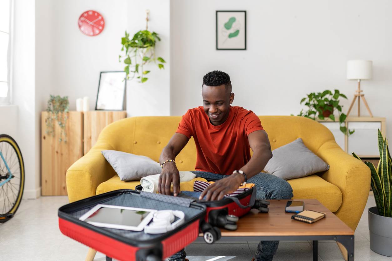 A man on the couch packing a red suitcase 