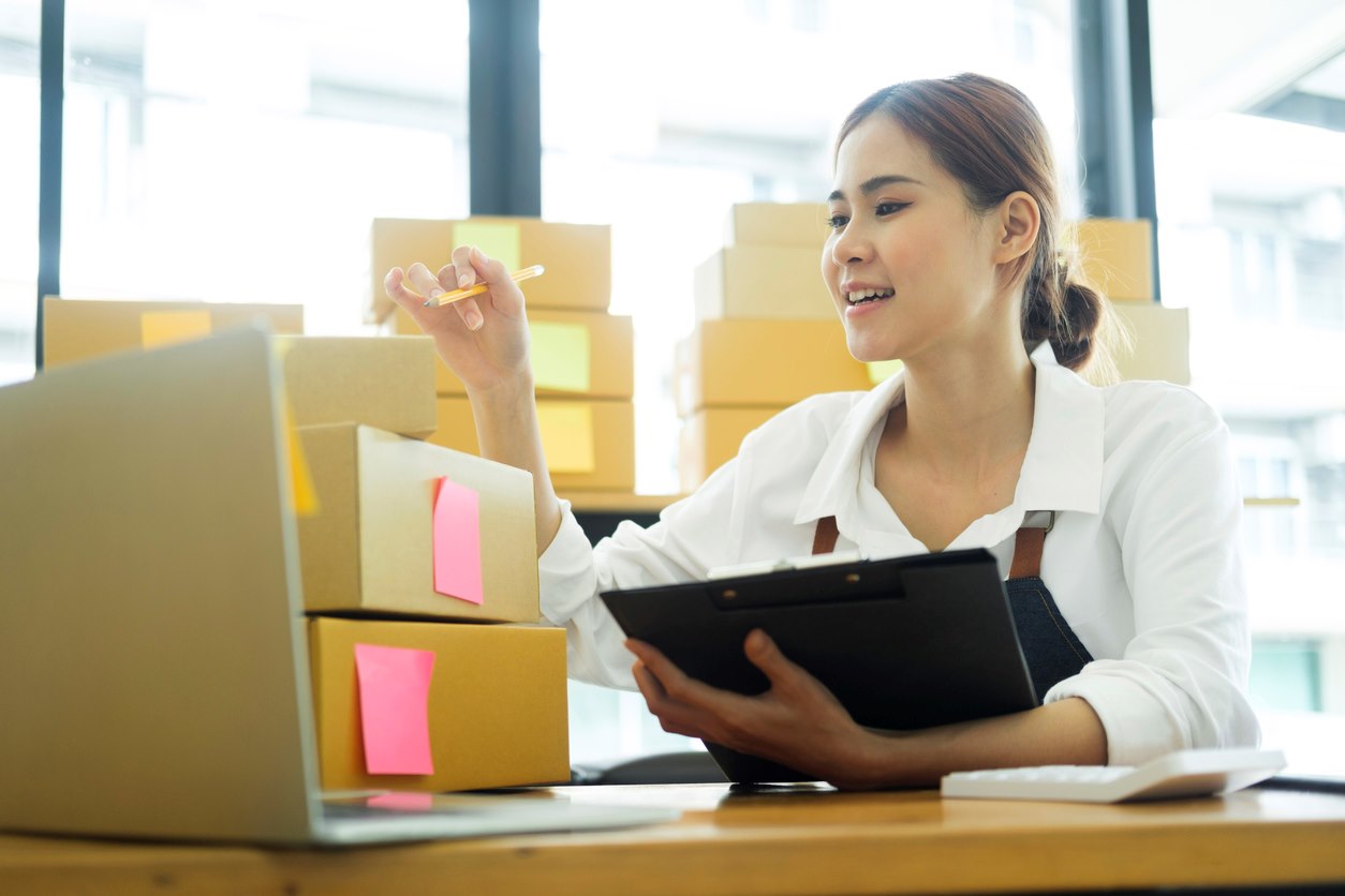 A woman sits at her desk writing on sticky note labels for boxes.