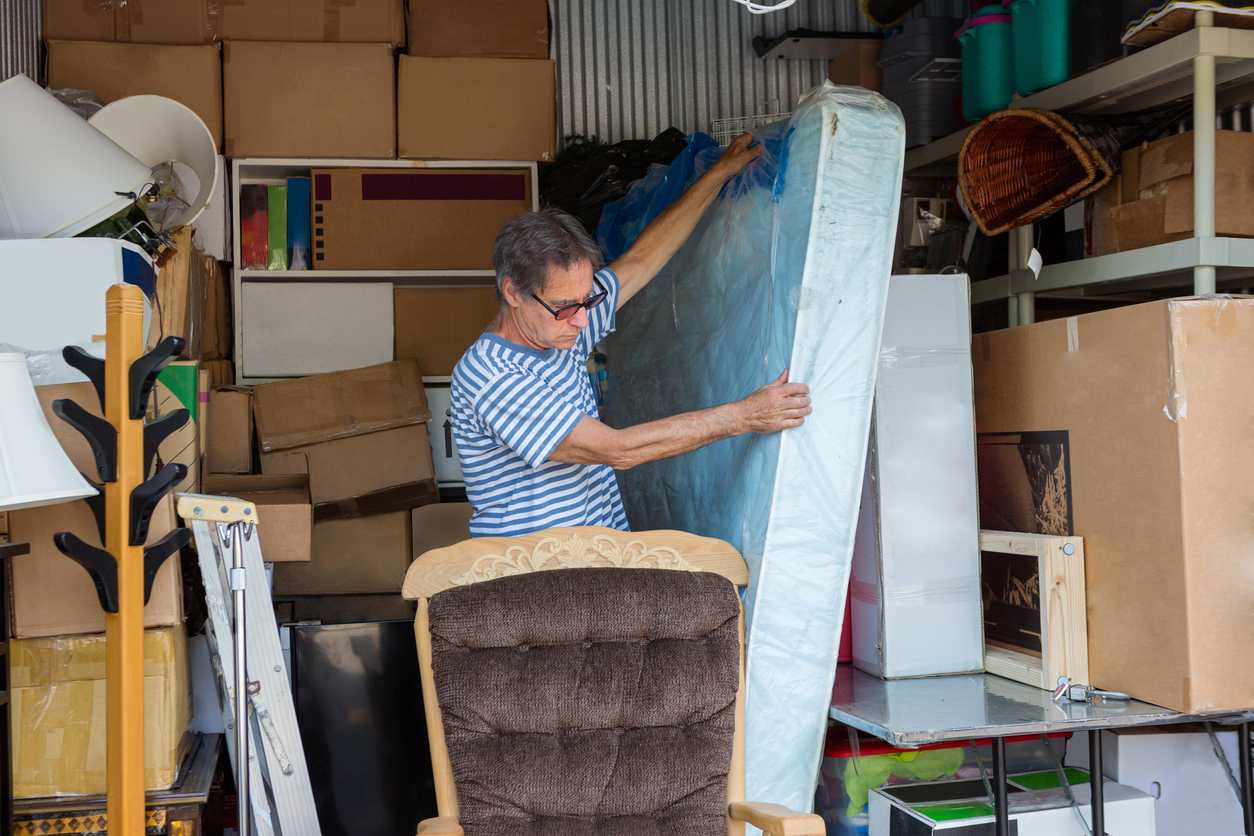 Man loading a mattress and other furniture items into a storage unit.