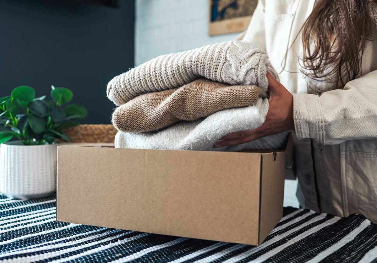 Woman placing clothing in a cardboard box in the middle of decluttering her home in the winter.