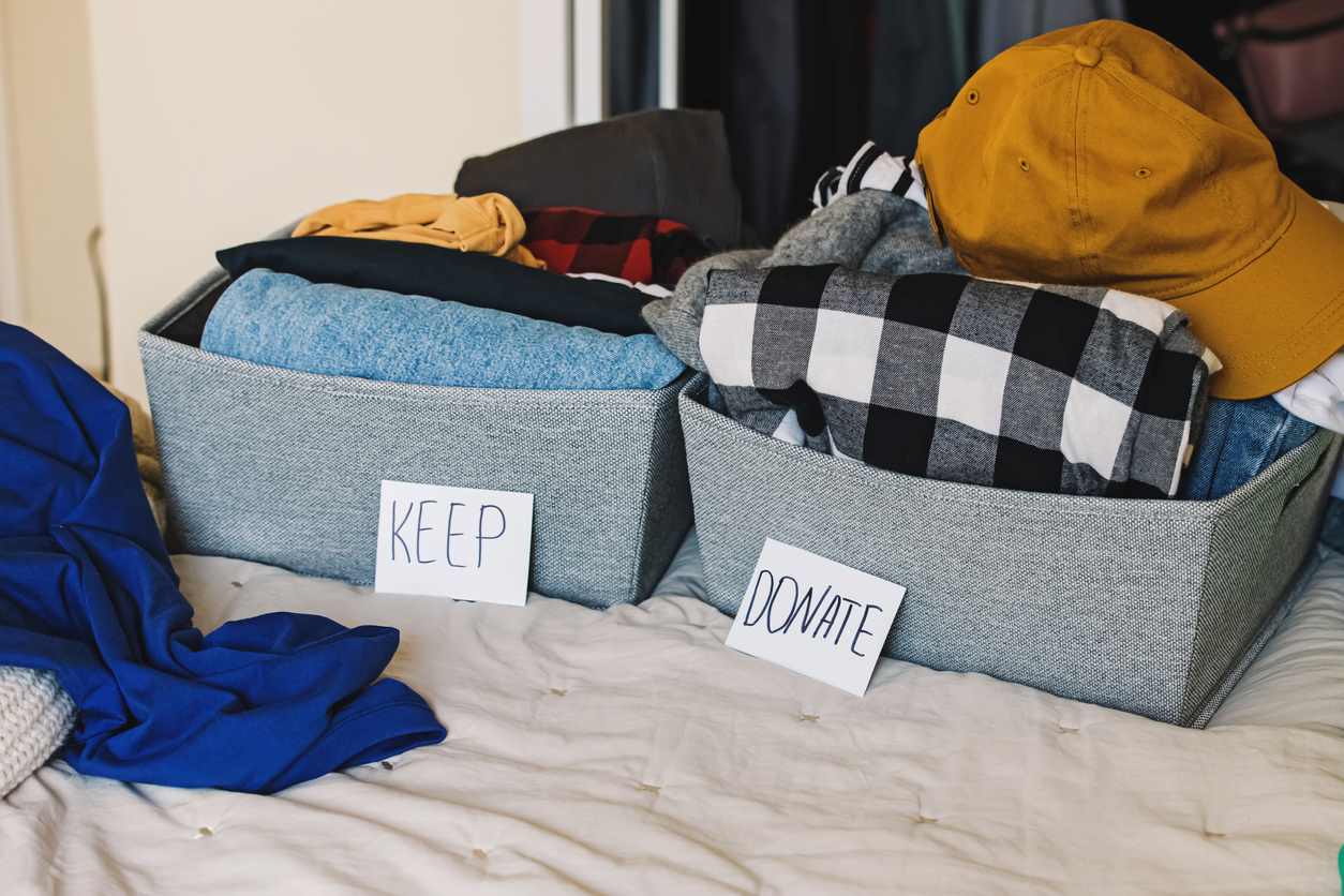Two piles of items organized in baskets labeled “keep” and “donate” on a bed.