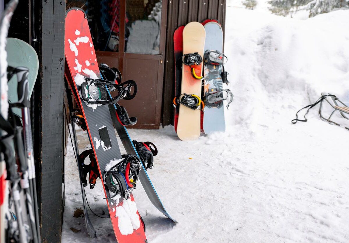 Winter gear, including snowboards, lying in snow near the entrance of a shed.