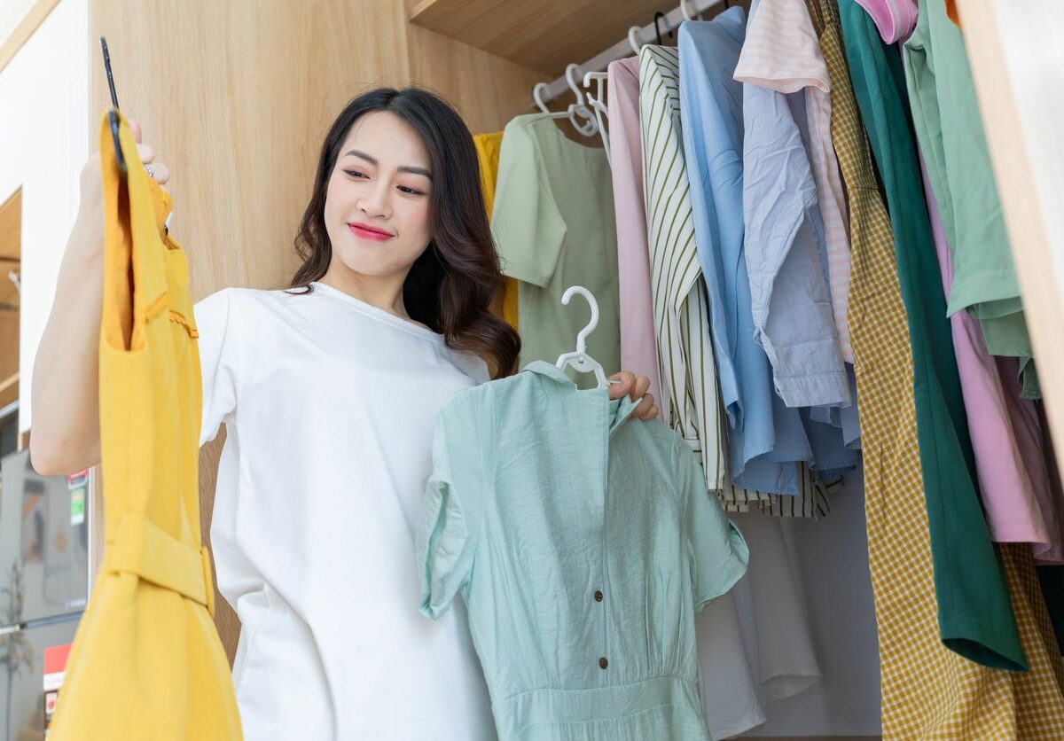 A young woman chooses clothes to keep in her closet based on seasonal wear.